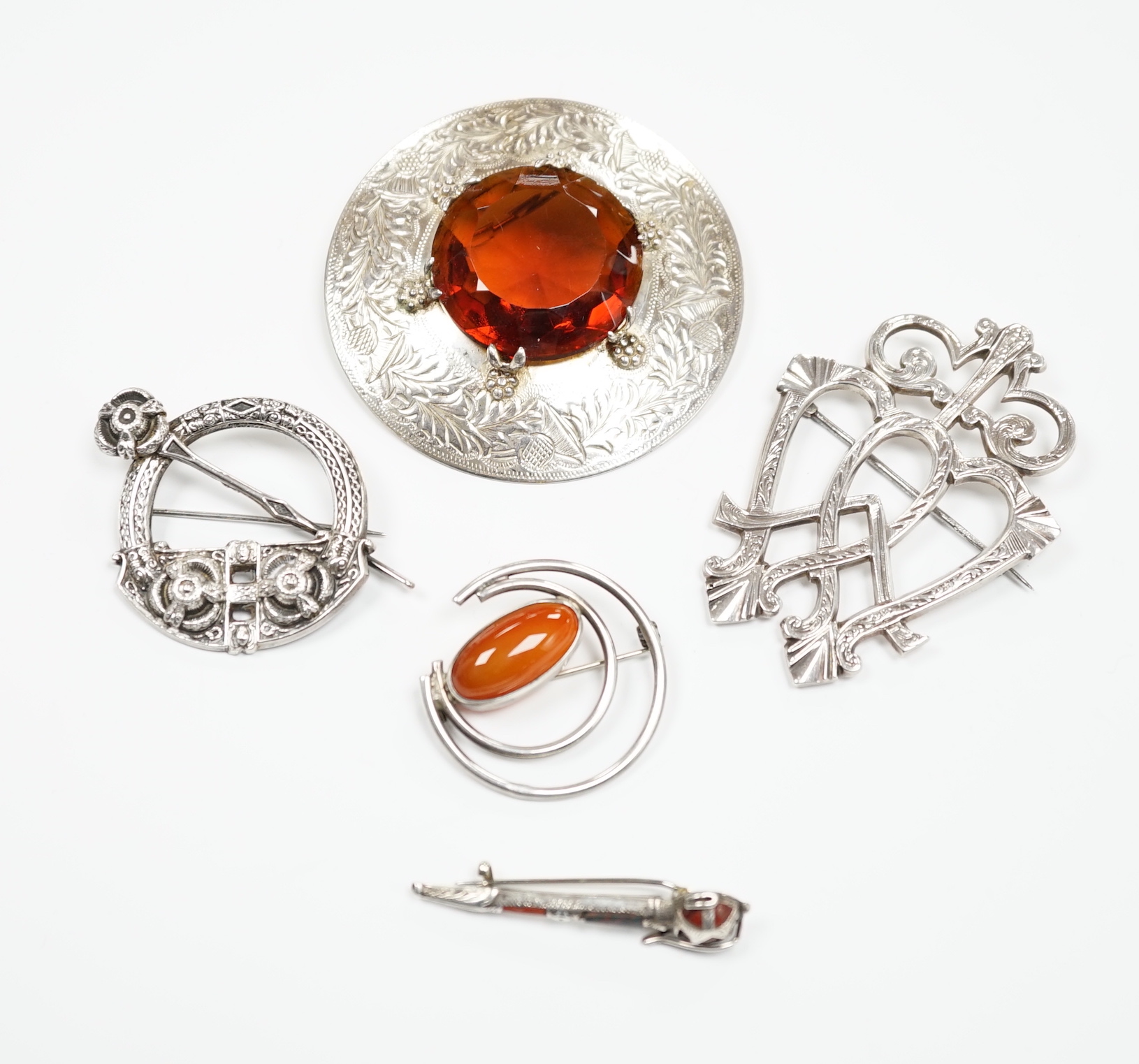 A 1950's Scottish silver and citrine coloured paste set circular brooch, 68mm, an Edwardian silver Celtic style brooch and three other white metal brooches, including Scottish hardstone set.